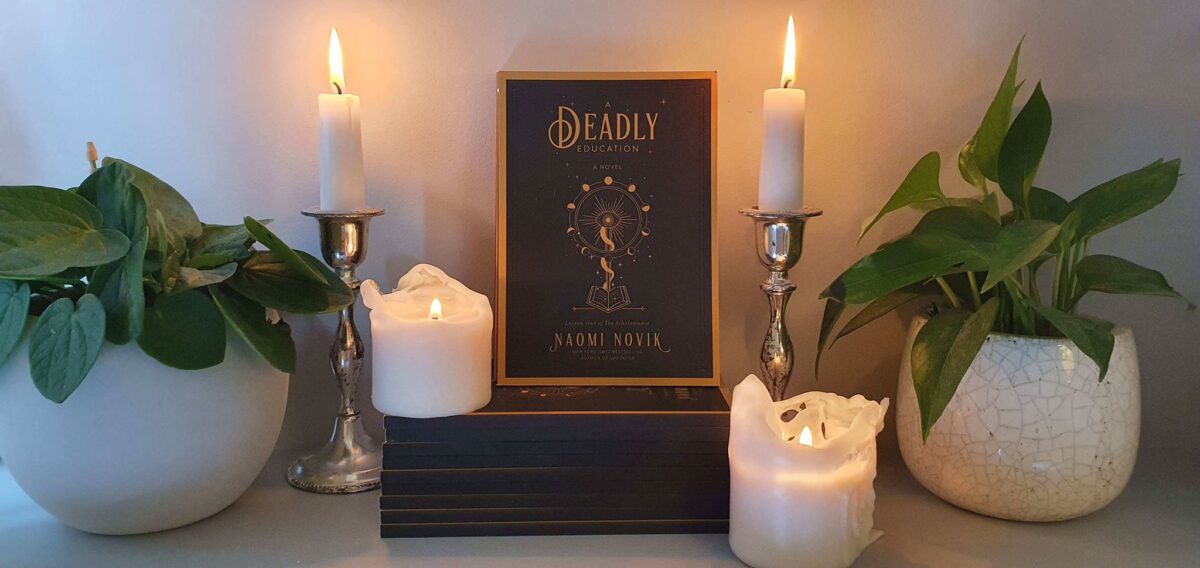 The book "A Deadly Education" propped up on a table with some candles and two potted plants